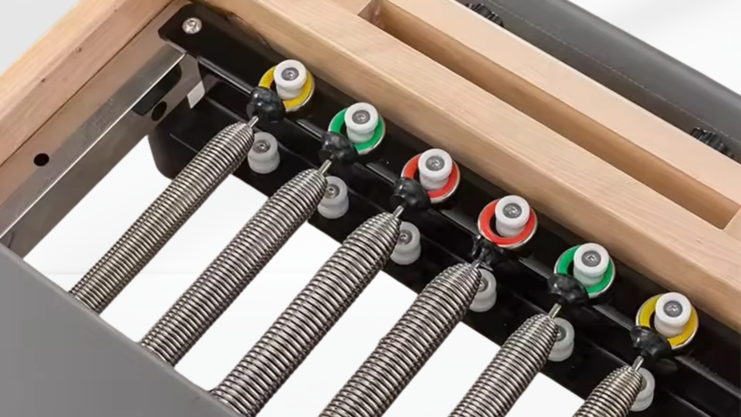 Close-up of a mechanical beige Pilates Reformer – Rebounder & 6-Level Resistance with springs and metal components on a wooden surface.