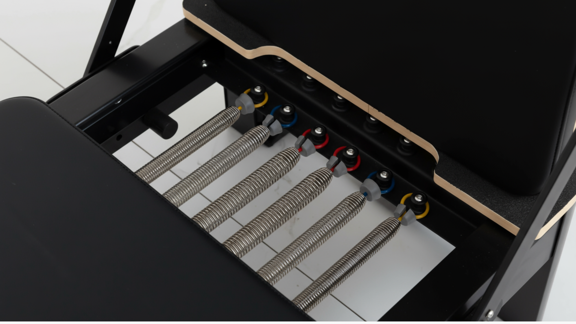 Close-up of a Pilates Reformer mechanical device with springs and gears on a white background