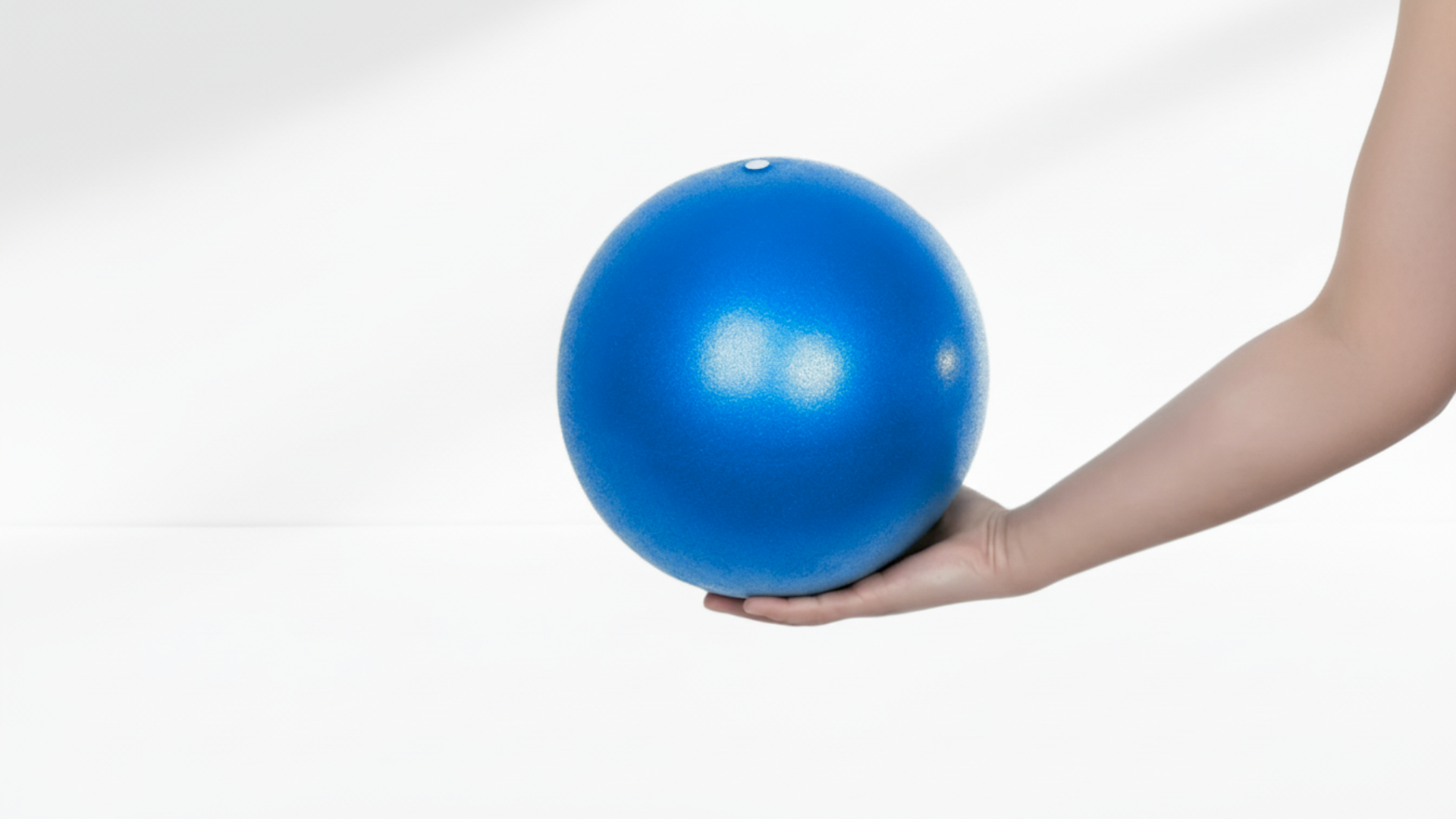 Hand holding a blue exercise ball against a white background