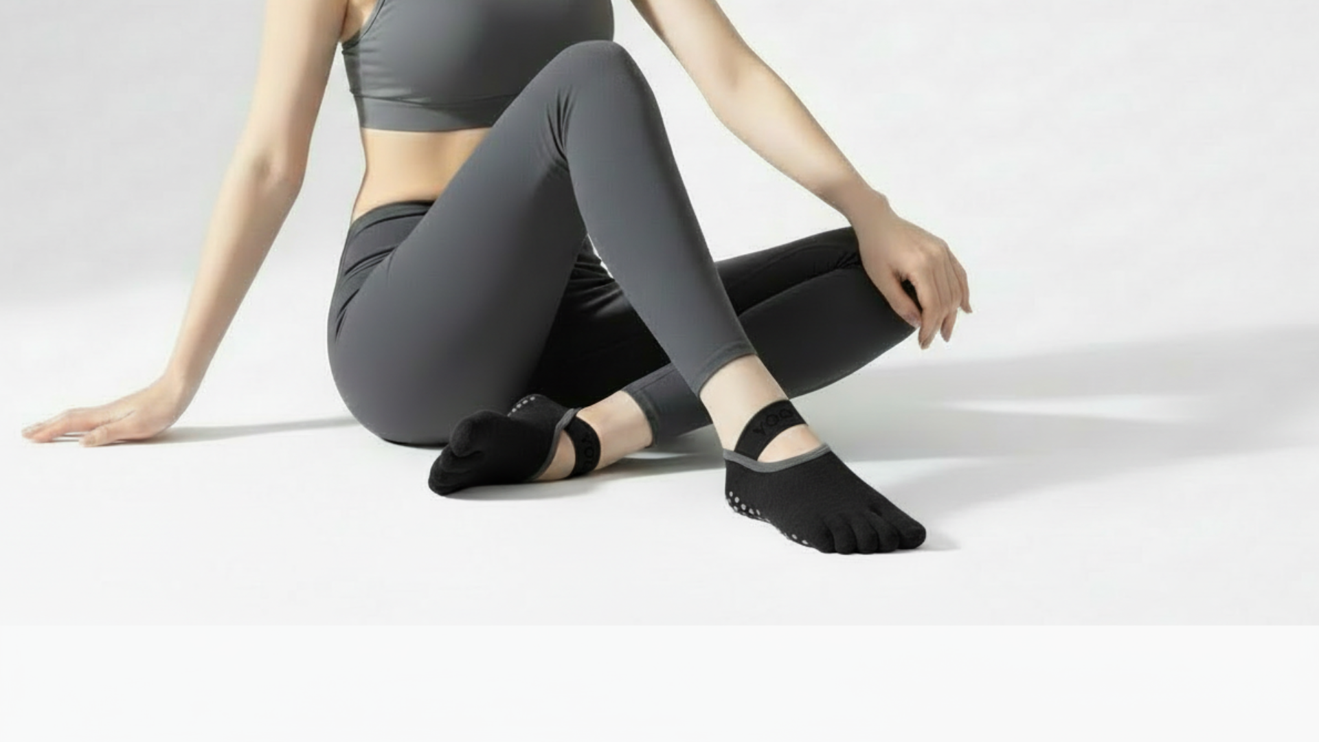 Person wearing a Toe Socks – Strap Edition gray leggings and black ballet flats sitting on a white surface