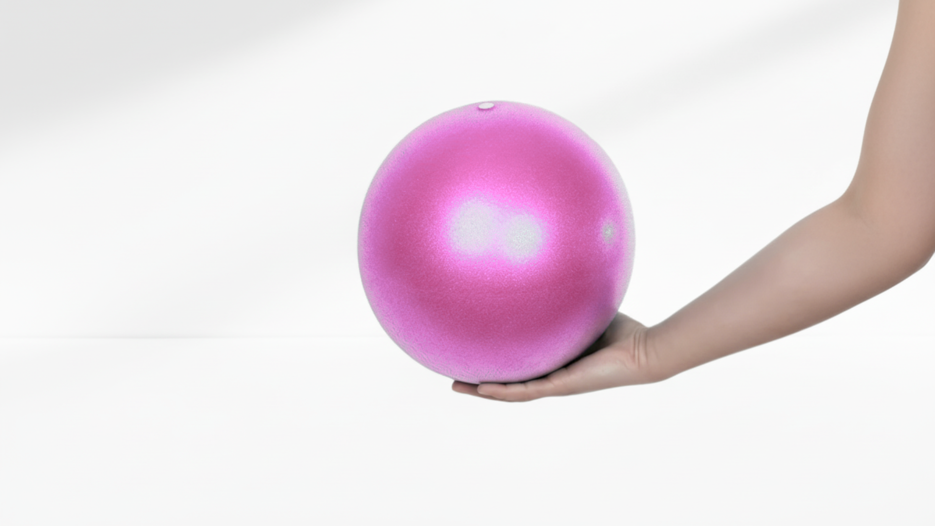Pink exercise ball held by a hand on a white background