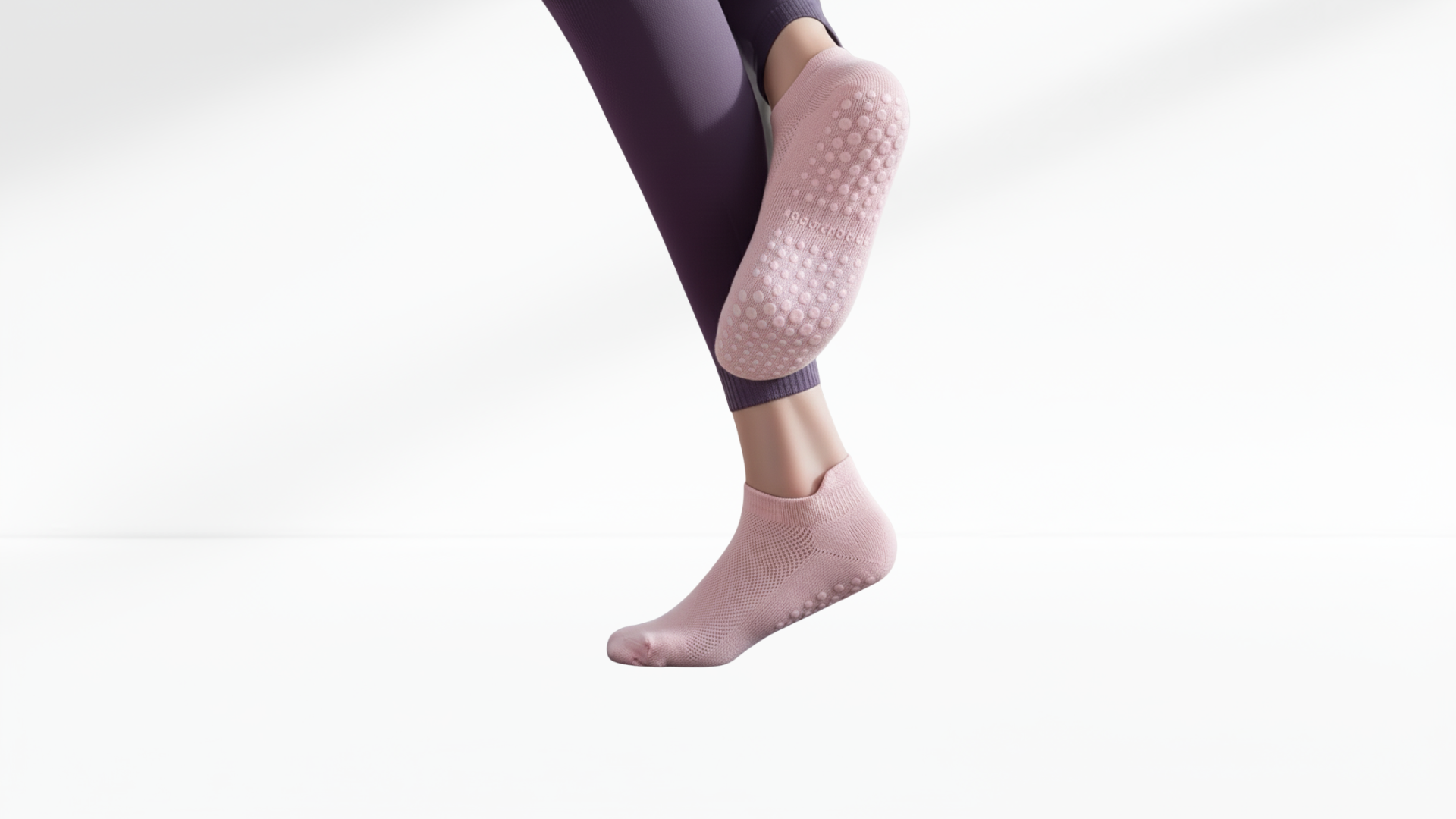 Pink grip socks with textured sole worn by a person on a white-grey background