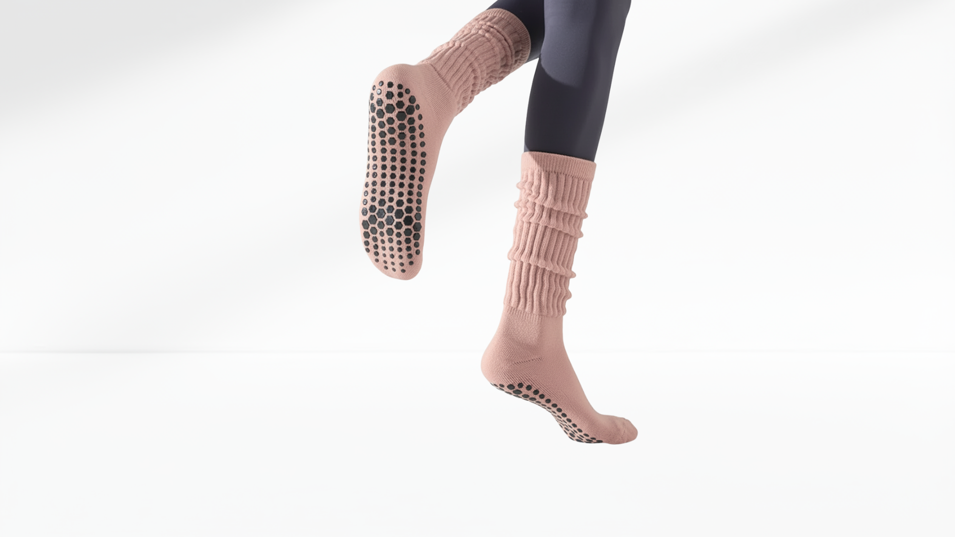 Pink yoga grip socks with grip dots worn by a person on a white-grey background
