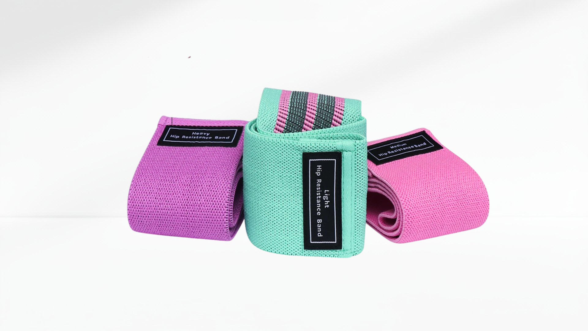 Three resistance bands in pink, green, and pink on a white-grey background