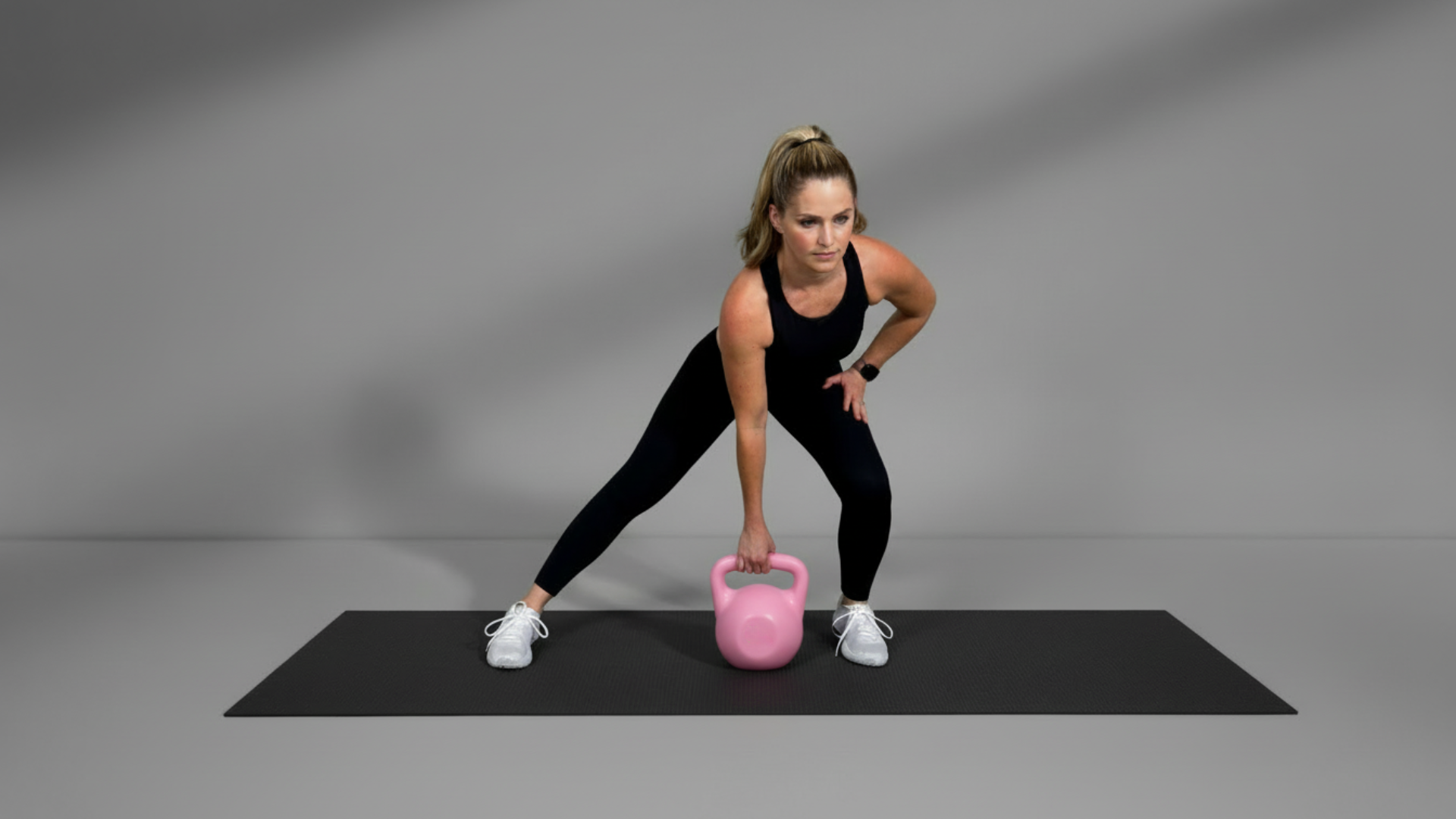 Woman exercising with a pink kettlebell on a gray background